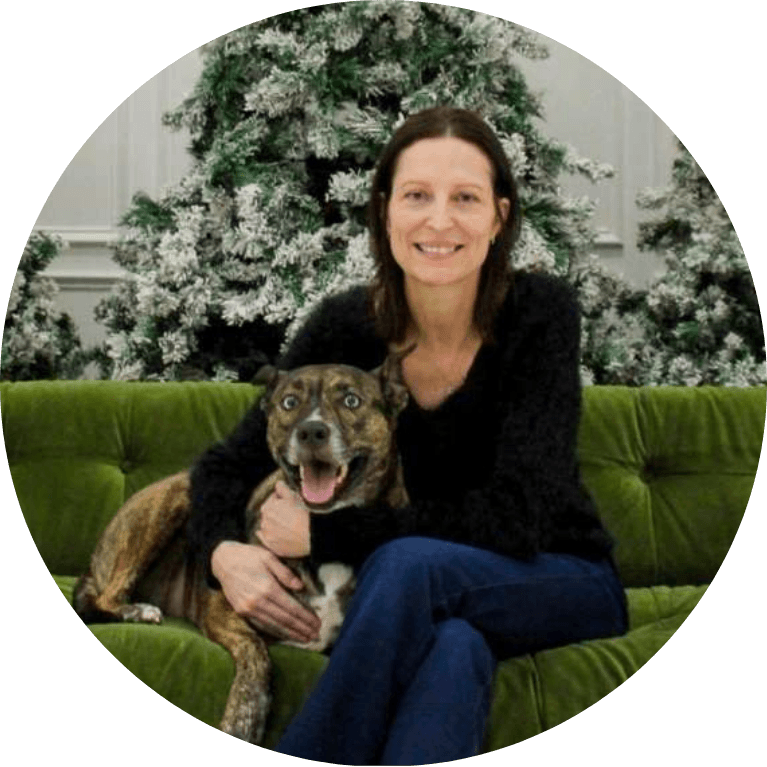 Staci sitting on green couch with a dog in her lap surrounded by frosty Christmas trees